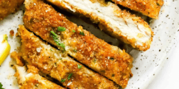 Close-up of crispy, baked chicken cutlets sliced into strips on a white plate, garnished with chopped parsley.