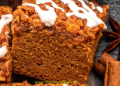 A close-up of a thick slice of pumpkin coffee cake, topped with streusel and white icing, is surrounded by cinnamon sticks and star anise. This pumpkin coffee cake looks perfectly spiced for autumn.