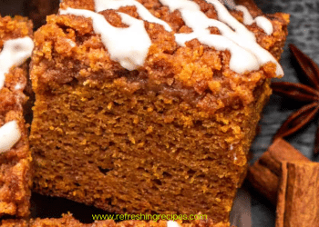 A close-up of a thick slice of pumpkin coffee cake, topped with streusel and white icing, is surrounded by cinnamon sticks and star anise. This pumpkin coffee cake looks perfectly spiced for autumn.