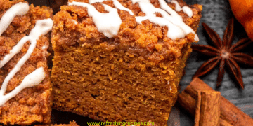 A close-up of a thick slice of pumpkin coffee cake, topped with streusel and white icing, is surrounded by cinnamon sticks and star anise. This pumpkin coffee cake looks perfectly spiced for autumn.