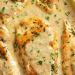 Golden brown Garlic Parmesan Chicken breasts covered in a creamy, herb-filled sauce, garnished with chopped parsley and served with lemon wedges.
