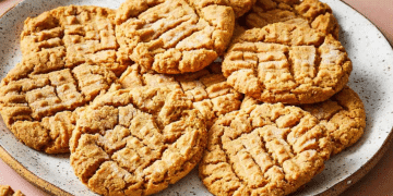 A plate filled with golden-brown peanut butter cookies, featuring a classic crisscross fork pattern on top. The cookies are arranged neatly and have a slightly crumbly texture, showcasing the timeless appeal of homemade peanut butter cookies.