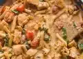 A creamy chicken pasta dish with penne, grilled chicken pieces, cherry tomatoes, and spinach, all mixed in a rich, seasoned sauce and stirred with a wooden spoon in a skillet.