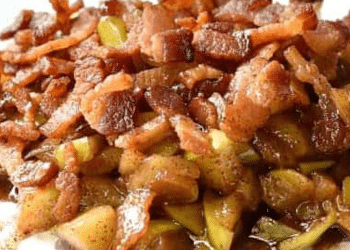 A close-up of Baked Brie topped with cooked bacon pieces and chopped apples, all covered in a brown, glossy sauce.