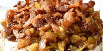 A close-up of Baked Brie topped with cooked bacon pieces and chopped apples, all covered in a brown, glossy sauce.