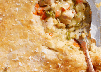 A close-up of a golden, flaky pot pie crust with a spoon scooping out creamy filling made of chicken, peas, carrots, and other vegetables—truly the best comfort food for any occasion.