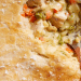 A close-up of a golden, flaky pot pie crust with a spoon scooping out creamy filling made of chicken, peas, carrots, and other vegetables—truly the best comfort food for any occasion.
