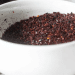 A close-up of a white bowl filled with ground sumac and ancho chili powder, both boasting rich colors and coarse textures, sitting on a light surface.