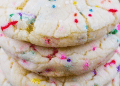 A close-up of stacked, soft cake mix cookies with colorful rainbow sprinkles, resting on a cooling rack.
