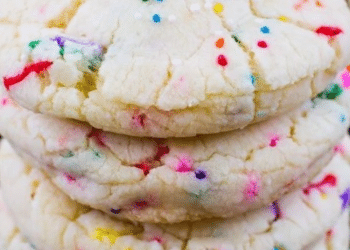 A close-up of stacked, soft cake mix cookies with colorful rainbow sprinkles, resting on a cooling rack.
