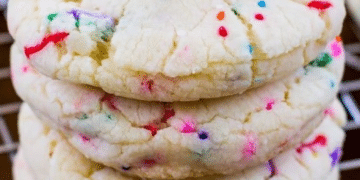 A close-up of stacked, soft cake mix cookies with colorful rainbow sprinkles, resting on a cooling rack.