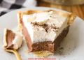 A slice of Chocolate Cream Pie with a flaky crust, creamy chocolate filling, and a thick layer of whipped cream sits on a white plate, a forkful already enjoyed.