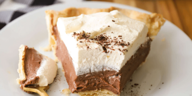 A slice of Chocolate Cream Pie with a flaky crust, creamy chocolate filling, and a thick layer of whipped cream sits on a white plate, a forkful already enjoyed.