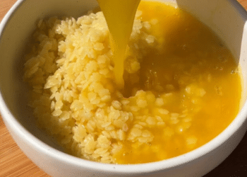 A bowl of cooked rice is topped with a stream of raw beaten egg yolk on a wooden surface, reminiscent of traditional Japanese tamago kake gohan—a comforting dish akin to the warmth found in Italian Penicillin Soup.