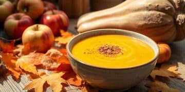 A bowl of creamy Apple Butternut Squash Soup is topped with spices and surrounded by autumn leaves, apples, and a butternut squash on a rustic wooden table, creating a cozy fall atmosphere.