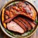 A bowl with a large, roasted, juicy piece of beef, partially sliced to reveal its tender pink interior—an ideal choice for Carnivore Diet Recipes. Garnished with fresh herbs, roasted carrot, and a sprig of rosemary.