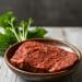 A wooden bowl holds a slice of uncooked, seasoned plant-based meat. Fresh green herbs are placed on the rustic wooden surface in the background, perfect for those exploring free carnivore diet recipes with a modern twist.