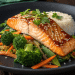 A plate with glazed miso salmon recipe garnished with sesame seeds and herbs, served over sautéed vegetables (broccoli, carrots, snap peas) and a side of white rice.