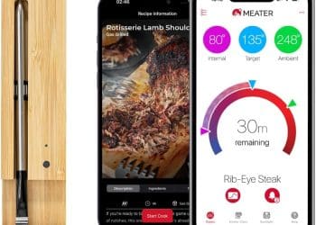 A MEATER+ Smart Meat Thermometer in a wooden charging case sits beside two smartphones displaying the MEATER app, showcasing cooking details and a temperature progress screen for a rib-eye steak.