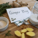 Fresh ginger root, sliced ginger, a jar of sugar, powdered ginger, herbs, and a spoon arranged on a wooden surface with a card labeled Ginger Bug—perfect ingredients for trying your own ginger bug recipe.