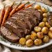 Sliced tender beef pot roast with carrots and potatoes on a white serving platter
