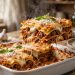 Slice of classic homemade beef lasagna with melted mozzarella and fresh basil in a white baking dish