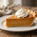 A slice of classic pumpkin pie topped with whipped cream on a white ceramic plate