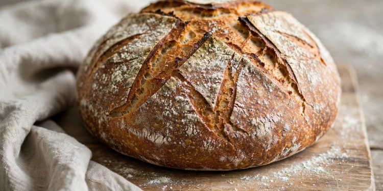 Rustic round sourdough loaf with a deeply scored golden crust cooling on a wooden board