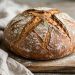 Rustic round sourdough loaf with a deeply scored golden crust cooling on a wooden board