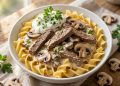 Creamy beef stroganoff with mushrooms over egg noodles in a white bowl