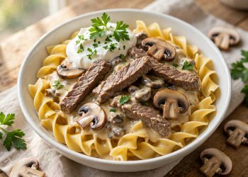 Creamy beef stroganoff with mushrooms over egg noodles in a white bowl