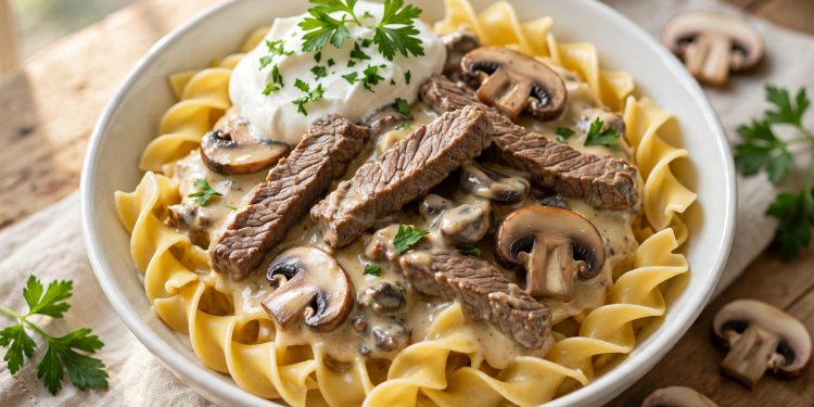 Creamy beef stroganoff with mushrooms over egg noodles in a white bowl