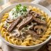 Creamy beef stroganoff with mushrooms over egg noodles in a white bowl