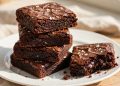 Stack of fudgy dark chocolate brownies with flaky sea salt on a white plate
