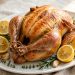 Whole golden lemon herb roast chicken with lemon halves and fresh herbs on a platter