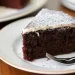 A slice of rich chocolate cake, inspired by Beatty's chocolate cake recipe, with a dusting of powdered sugar and a layer of white icing on top, served on a white plate with a fork.