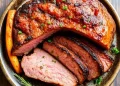 A bowl with a large, roasted, juicy piece of beef, partially sliced to reveal its tender pink interior—an ideal choice for Carnivore Diet Recipes. Garnished with fresh herbs, roasted carrot, and a sprig of rosemary.