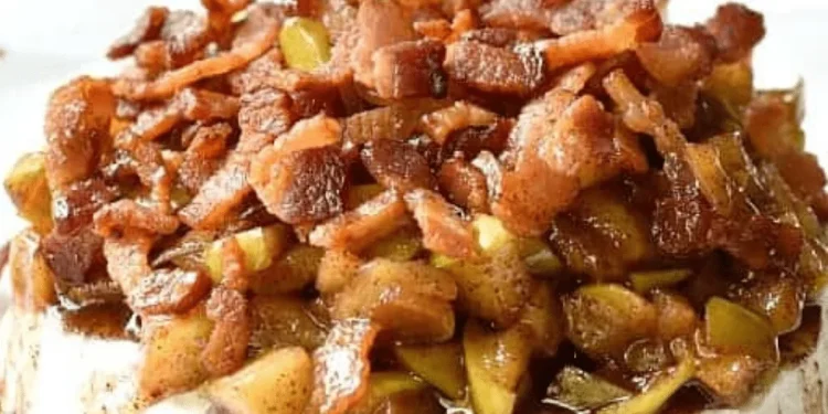 A close-up of Baked Brie topped with cooked bacon pieces and chopped apples, all covered in a brown, glossy sauce.