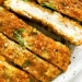 Close-up of crispy, baked chicken cutlets sliced into strips on a white plate, garnished with chopped parsley.