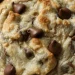 A close-up of a freshly baked chocolate chip cookie made with a Crumbl Cookie Recipe, featuring golden edges and melted chocolate chips on top, resting on a baking sheet.