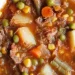 A bowl of old fashioned vegetable beef soup filled with hearty chunks of beef, potatoes, peas, carrots, corn, and green beans in a rich tomato-based broth.