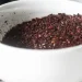 A close-up of a white bowl filled with ground sumac and ancho chili powder, both boasting rich colors and coarse textures, sitting on a light surface.