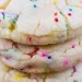 A close-up of stacked, soft cake mix cookies with colorful rainbow sprinkles, resting on a cooling rack.