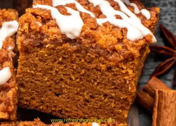A close-up of a thick slice of pumpkin coffee cake, topped with streusel and white icing, is surrounded by cinnamon sticks and star anise. This pumpkin coffee cake looks perfectly spiced for autumn.
