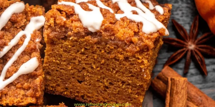 A close-up of a thick slice of pumpkin coffee cake, topped with streusel and white icing, is surrounded by cinnamon sticks and star anise. This pumpkin coffee cake looks perfectly spiced for autumn.