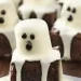 Chocolate mini cakes decorated as ghosts with draped white icing and chocolate dots for eyes and mouths, arranged on a wooden surface—perfect for fun Recipes with 3 Ingredients for your next spooky celebration.