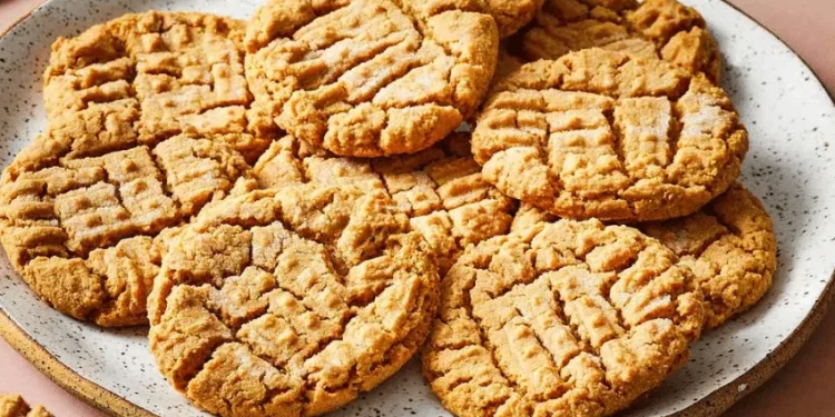 A plate filled with golden-brown peanut butter cookies, featuring a classic crisscross fork pattern on top. The cookies are arranged neatly and have a slightly crumbly texture, showcasing the timeless appeal of homemade peanut butter cookies.