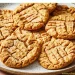 A plate filled with golden-brown peanut butter cookies, featuring a classic crisscross fork pattern on top. The cookies are arranged neatly and have a slightly crumbly texture, showcasing the timeless appeal of homemade peanut butter cookies.