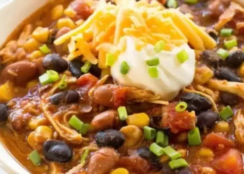 A close-up of a bowl of chicken taco soup with black beans, corn, tomatoes, and shredded chicken—this Taco Soup recipe is topped with sour cream, cheddar cheese, and chopped green onions.