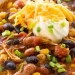 A close-up of a bowl of chicken taco soup with black beans, corn, tomatoes, and shredded chicken—this Taco Soup recipe is topped with sour cream, cheddar cheese, and chopped green onions.